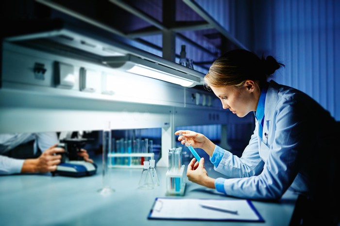 A lab research technician examining blue liquid in a test tube.