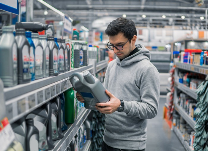 A customer in an auto parts store looks at a product container while standing in an aisle full of products